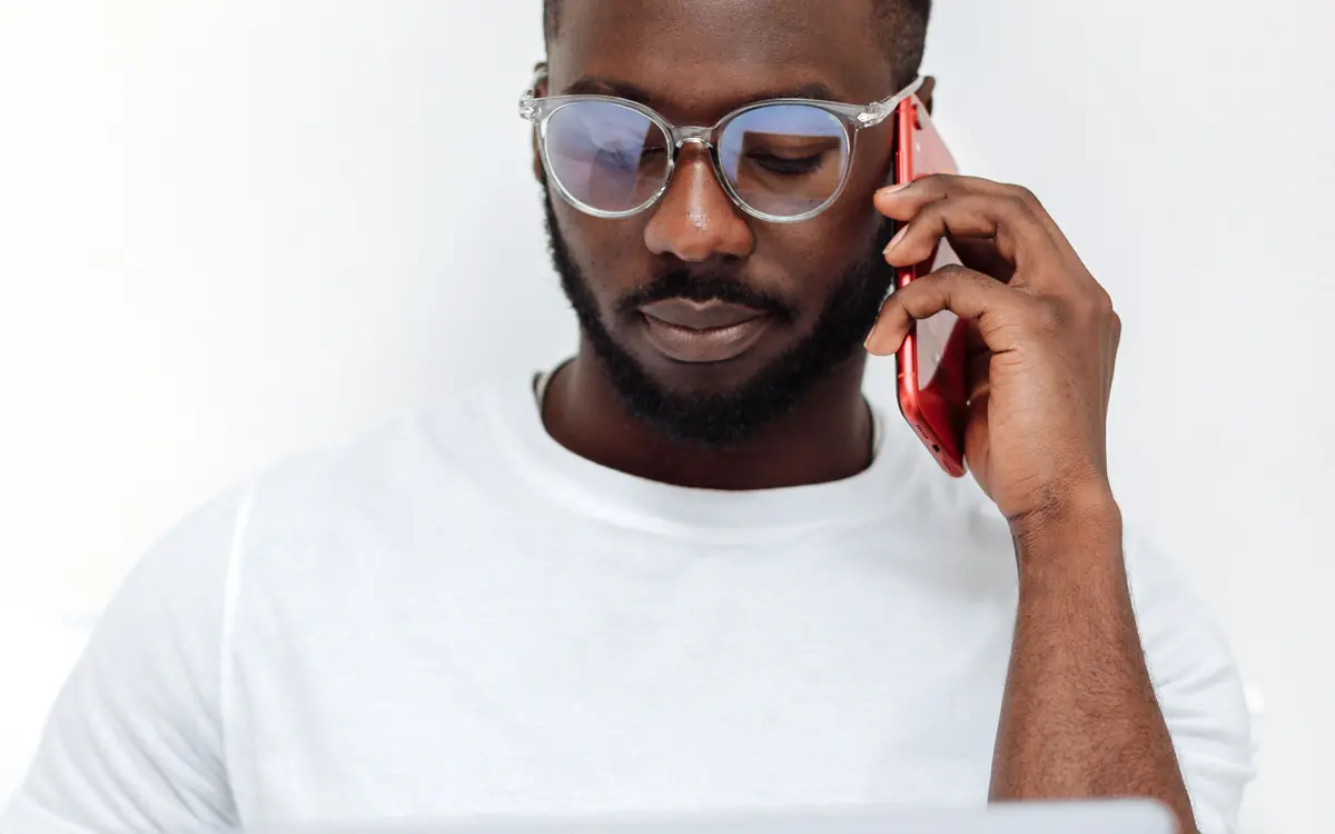 Homem em casa, com o notebook no colo, falando ao telefone